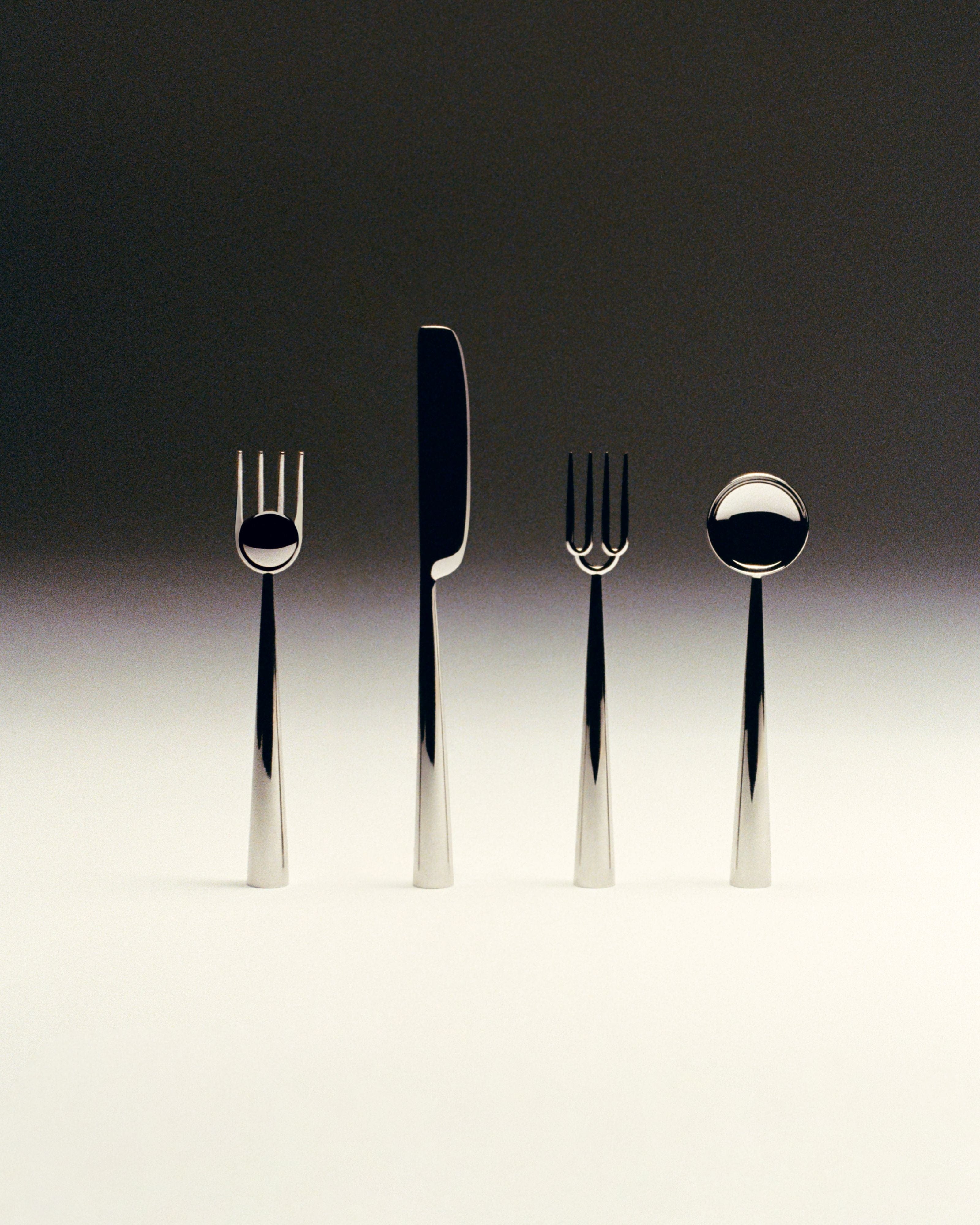 The ACC - Cutlery Set features four pieces—two forks, a knife, and a spoon—with modern, reflective finishes and thick cylindrical handles, making it an ideal minimalist housewarming gift.
